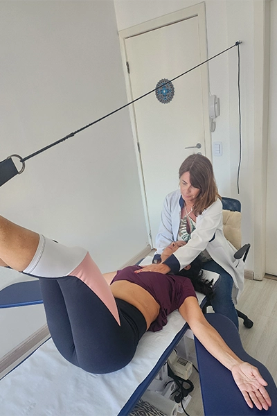 fisioterapeuta jenny realizando rpg na paciente, deitada, com as pernas sustentadas no ar
