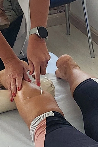 a mão da fisioterapeuta jenny realizando crochetagem na panturrilha de uma paciente, deitada
